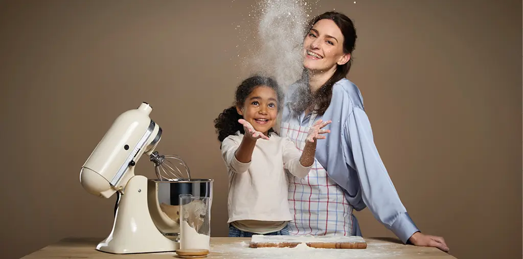 Mutter und Kind backen gemeinsam in der Küche, Mehl wirbelt durch die Luft und sorgt für spielerische Momente. Die Szene steht für Familienleben, Freude am Kochen und eine moderne wohnliche Küche mit Wohlfühlatmosphäre.